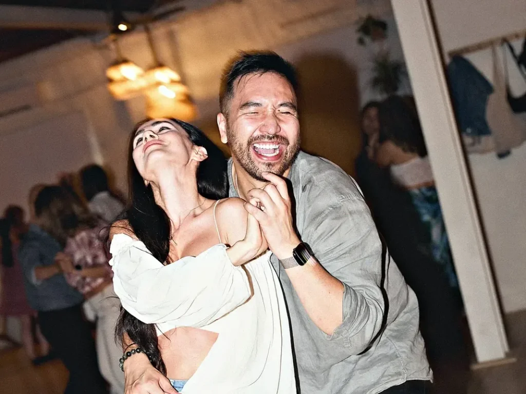 A couple laughing as they dance at a busy Beach Ballroom social