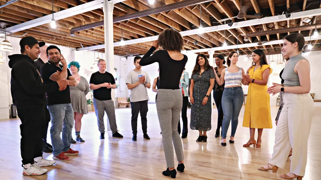 Students standing in a loose circle on the studio floor, chatting before class at Beach Ballroom
