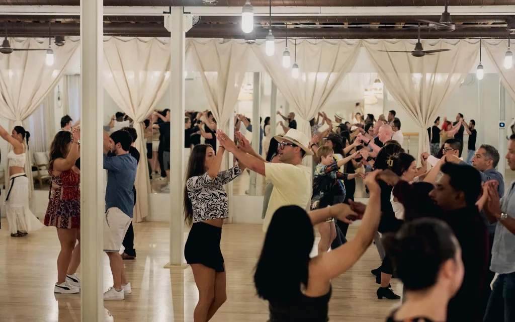 A full Latin class at Beach Ballroom, students raising their arms through a turn under the white columns