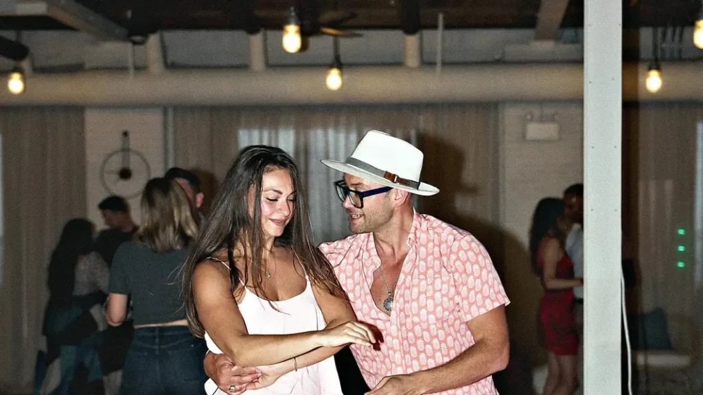 A couple partner dancing at a Latin social, her white dress swinging as they move