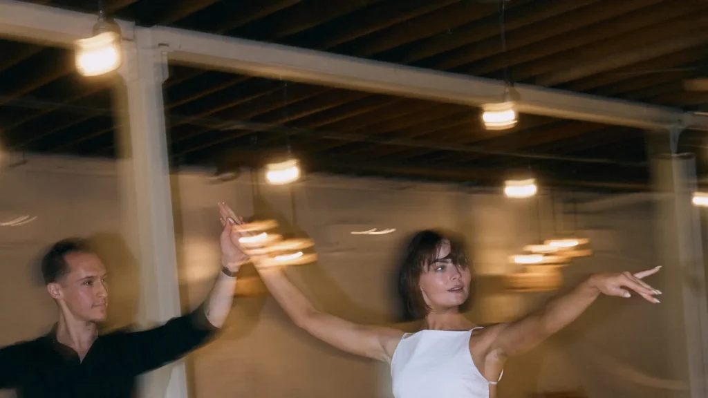 A couple opening out of hold with arms extended, her red trousers a blur, at a Beach Ballroom social