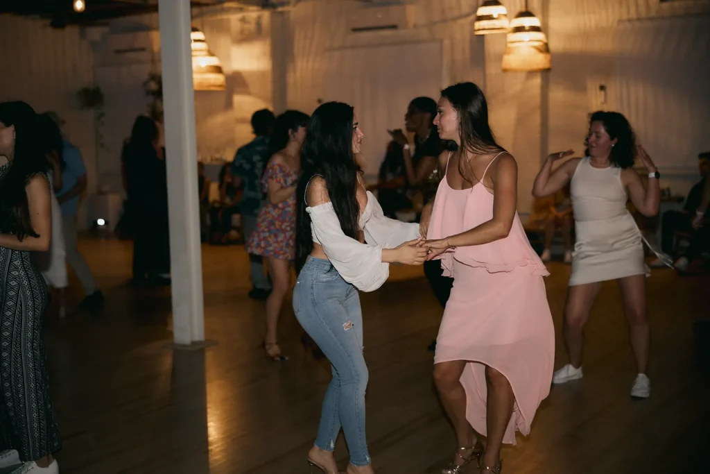 Two dancers laughing mid-turn at a Latin Thursday social, other couples dancing behind them