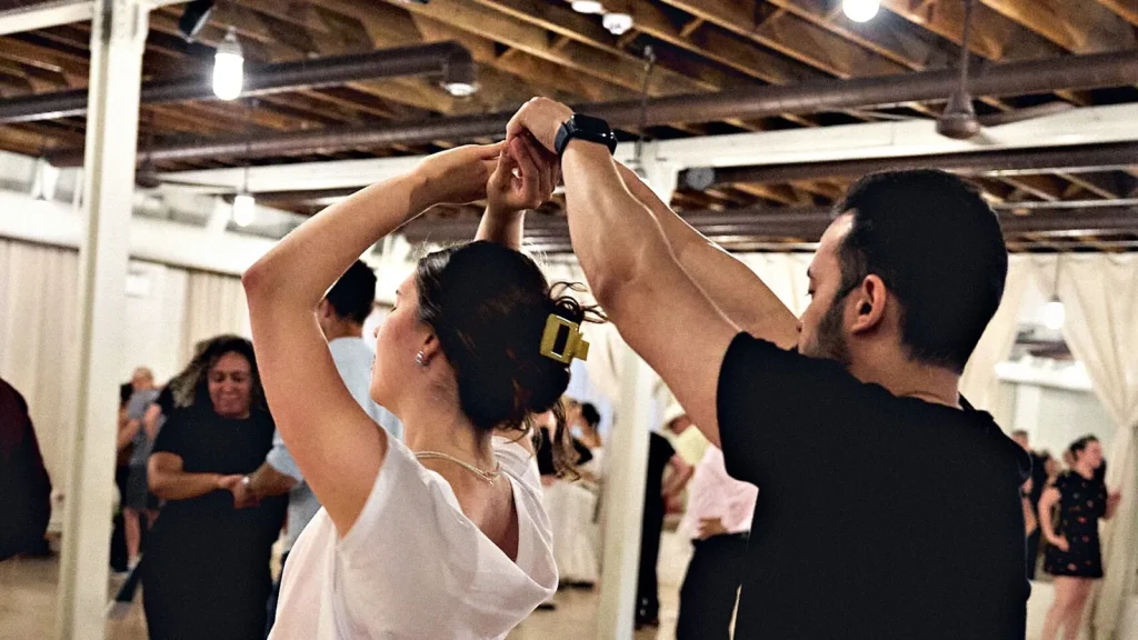 A lead raising his partner's hand into a turn on a crowded Beach Ballroom social floor